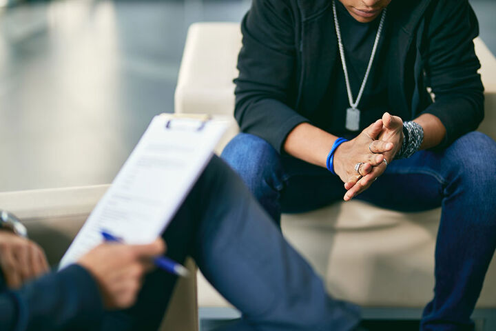 A student sits across from a counselor who is taking notes on a clipboard.